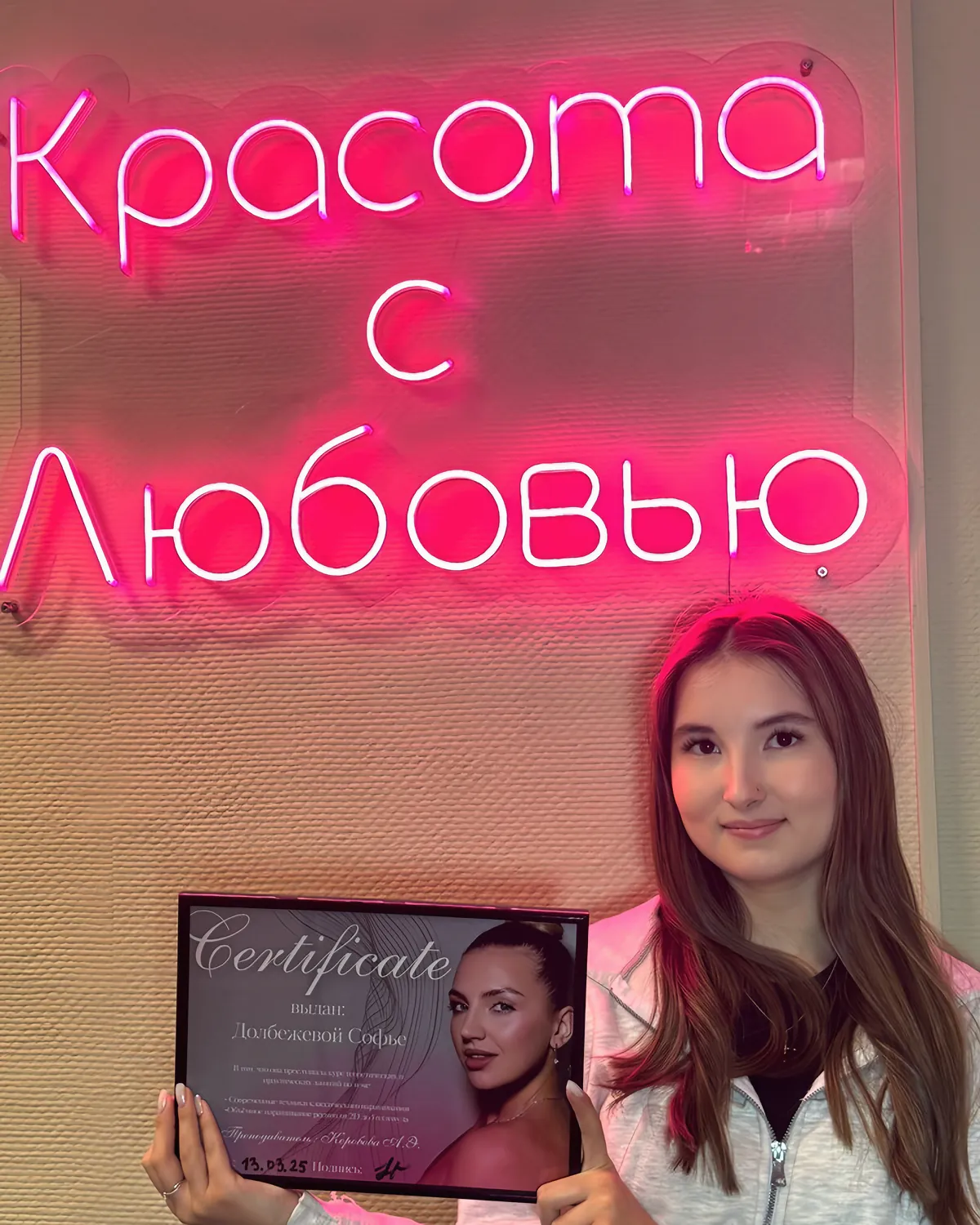 Выпускница курса с сертификатом под неоновой вывеской «Красота с любовью»